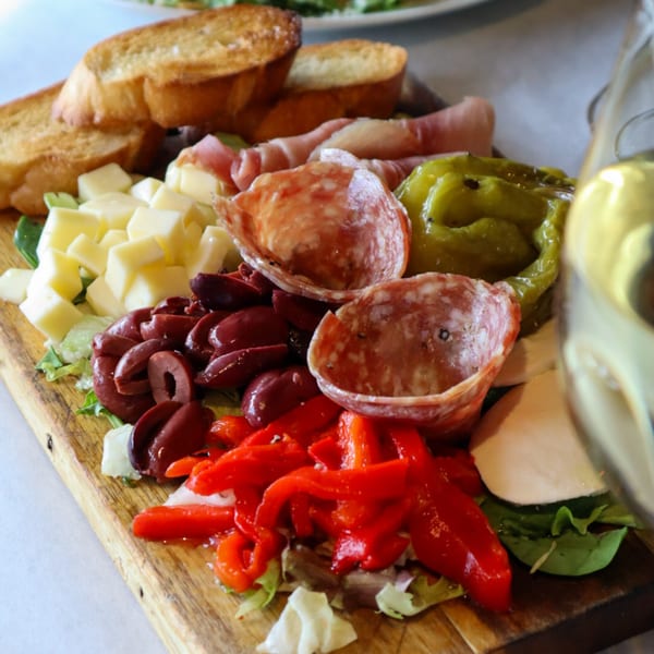 A Bacco Bistro charcuterie board with meats, cheeses, olives, peppers, and toasted bread.