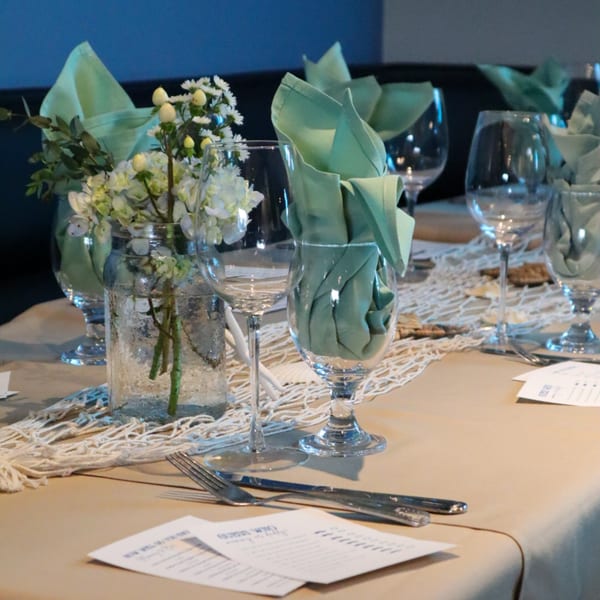A set table at Bacco Bistro with light green napkins, wine glasses, and a floral centerpiece.