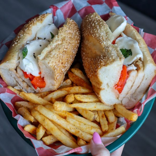 Two Italian chicken sandwiches with fresh mozzarella, roasted red peppers, and basil, served with fries.