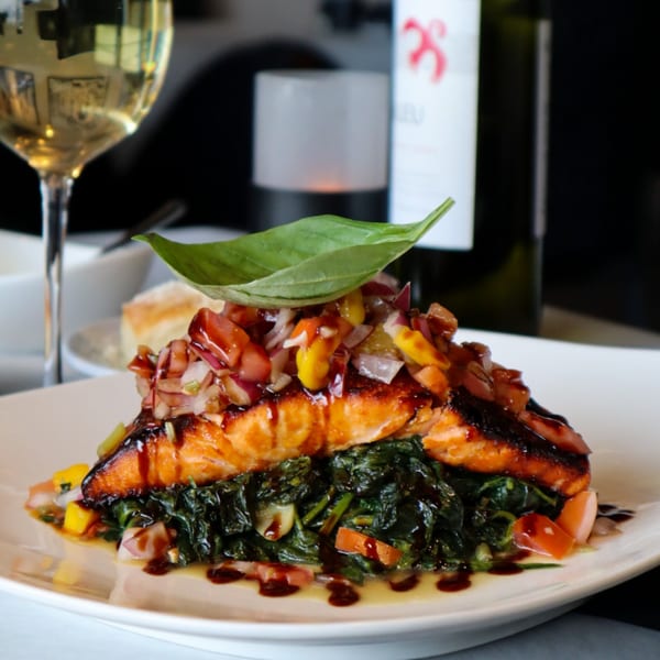 Grilled salmon with salsa, spinach, and balsamic glaze, served with wine at Bacco Bistro.