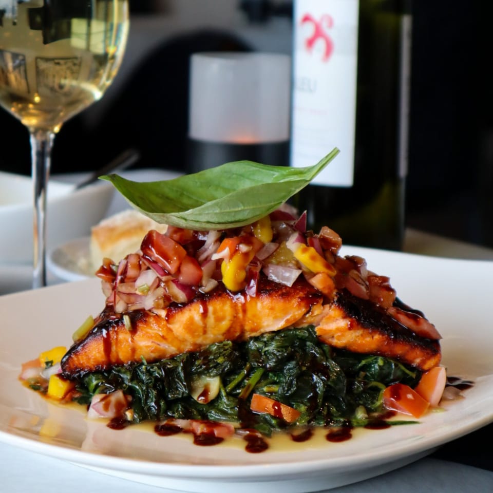 Grilled salmon with salsa, spinach, and balsamic glaze, served with wine at Bacco Bistro.