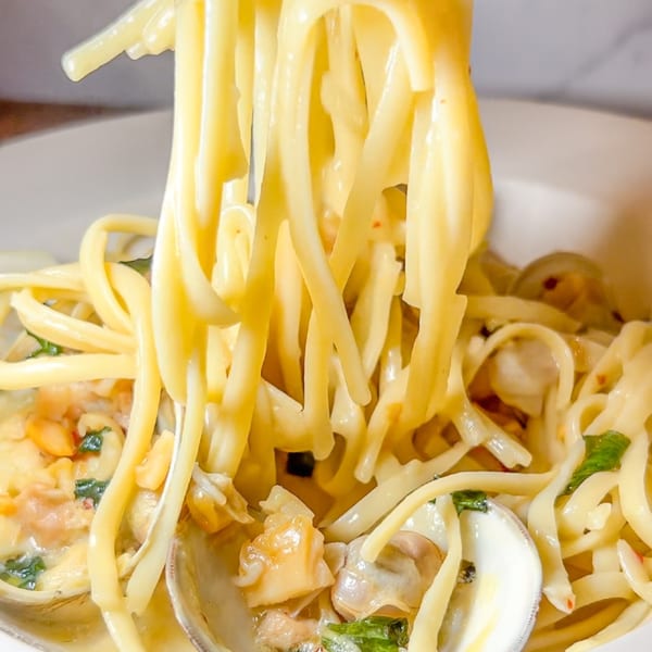 Close-up of linguine with clams, garlic, and herbs being lifted from a white bowl.