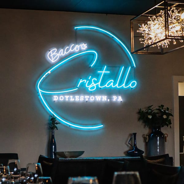Bacco Cristallo Doylestown, PA neon sign glowing blue on a wall above a dining table.