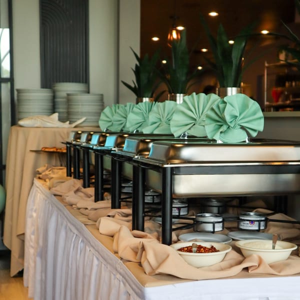 A buffet line with chafing dishes, neatly folded green napkins, and bowls of spices at Bacco Bistro.