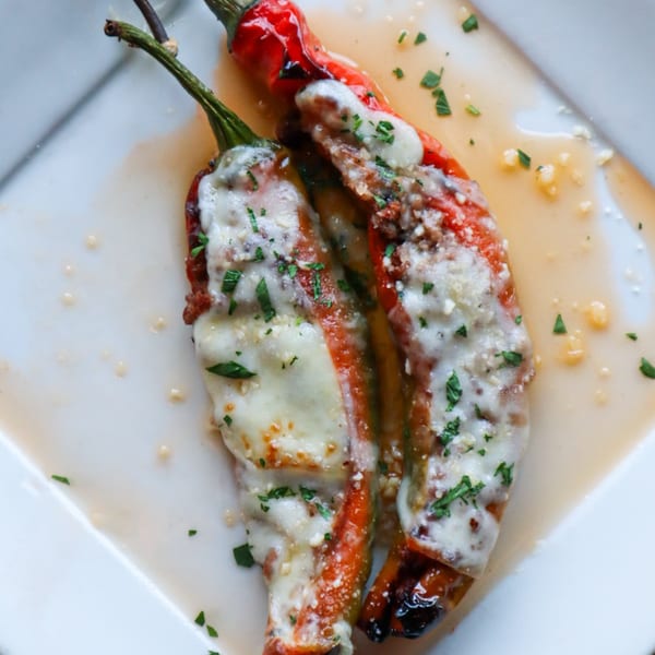 Two red peppers stuffed with meat and cheese, garnished with parsley, on a white plate.