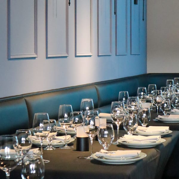 Set tables with wine glasses, plates, and napkins line a dark booth at Bacco Bistro.