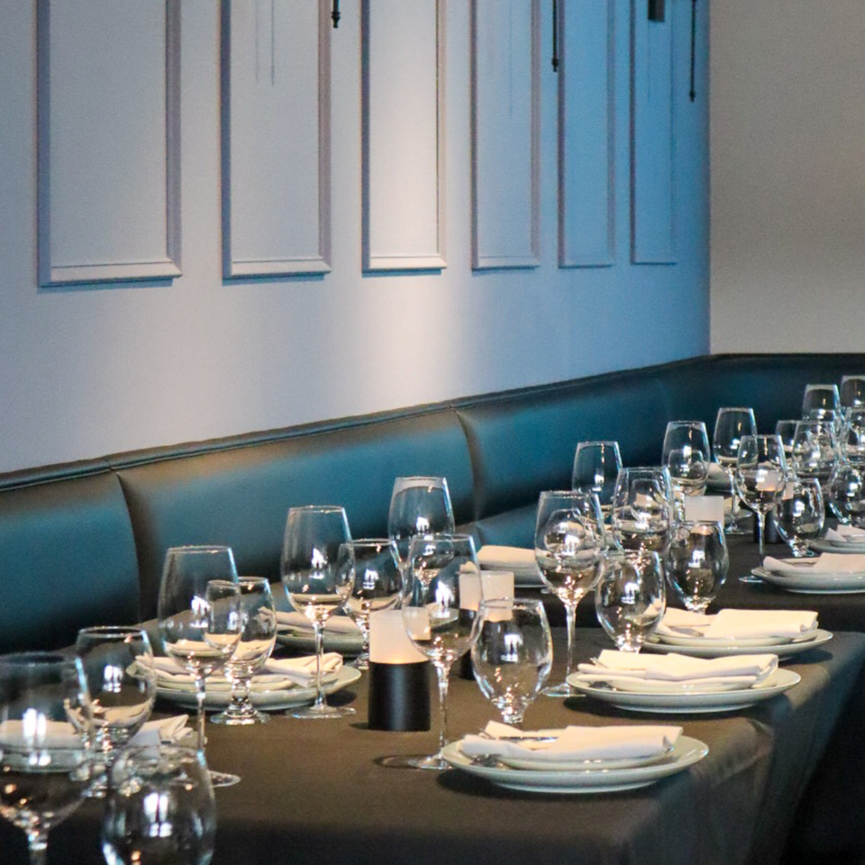 Set tables with wine glasses, plates, and napkins line a dark booth at Bacco Bistro.